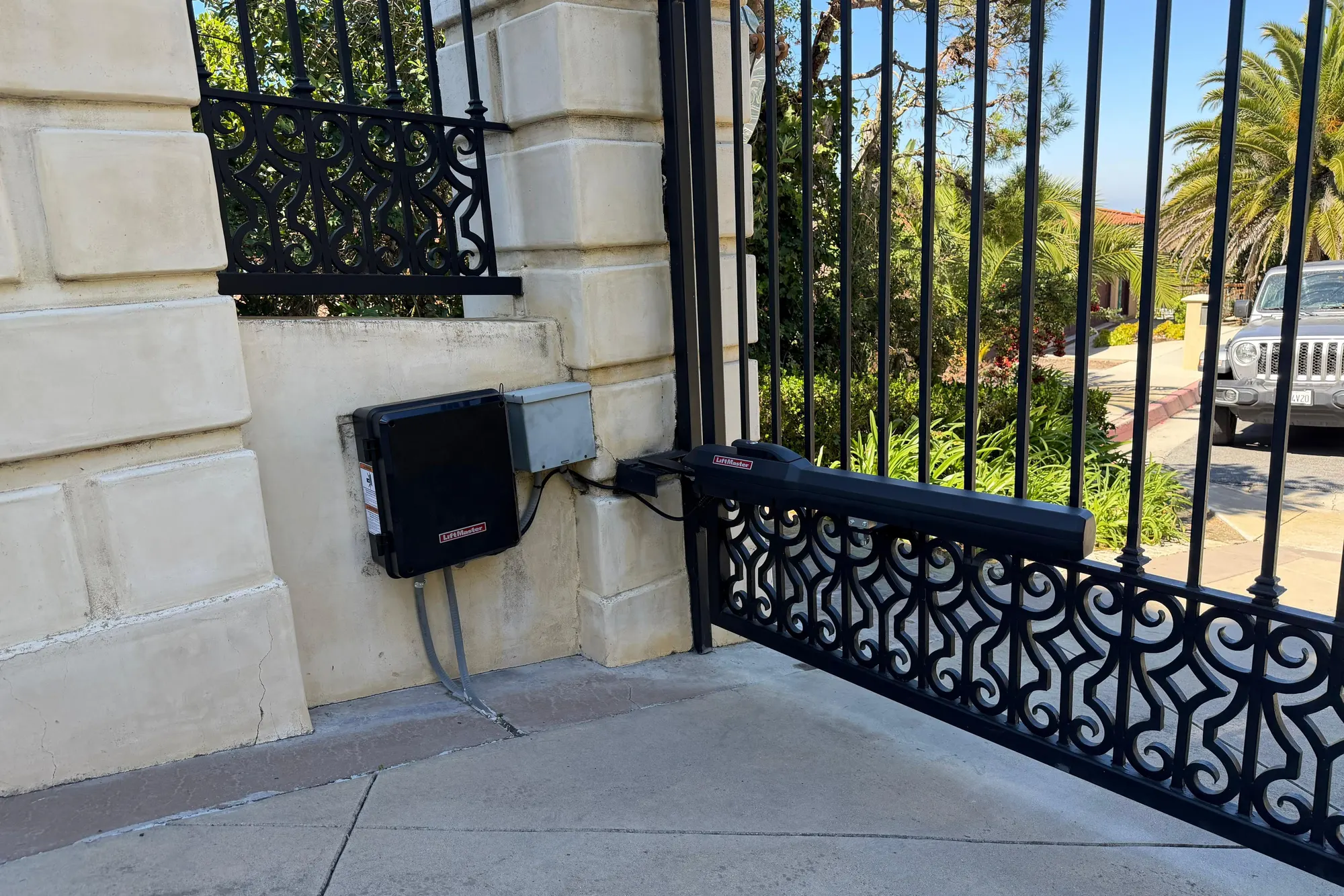A LiftMaster swing gate operator and its control box mounted beside a stone gate pillar