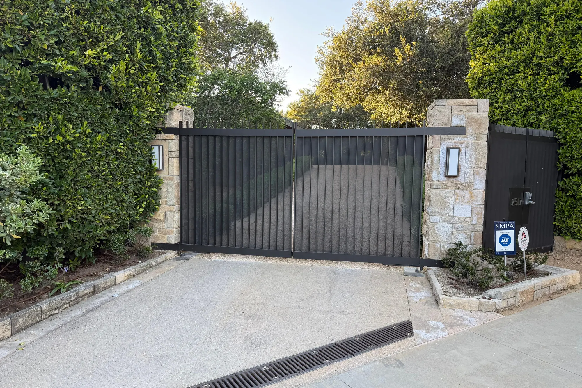 A dark metal estate driveway gate closed between stone pillars, fitted with a concealed gate operator