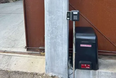 A photo-eye safety sensor mounted on a gate post, aligned across a driveway opening