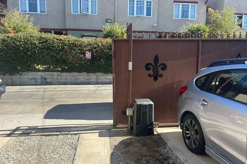A swing gate operator fitted to a brown metal driveway gate beside a parked car