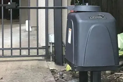A solar charging panel mounted near a gate operator on a rural driveway